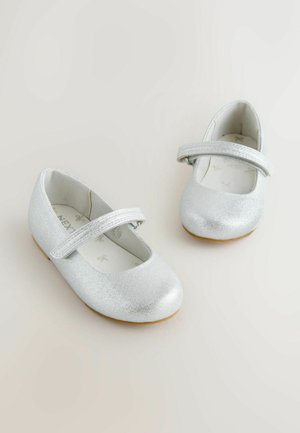 Balletflade sko i sølv med rundet tå, flad sål og justerbar rem over foden. Glat tekstur med diskret glans.