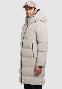 Lys grå pufferjakke med hætte, udstyret med lynlås foran, to sidelommer med lynlås og et logomærke ved kanten. Tekstureret, isoleret design.