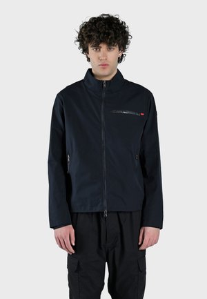 Giacca leggera blu navy con colletto alto, chiusura con zip e tasche laterali. Presenta una stampa del logo sul petto e una texture morbida.