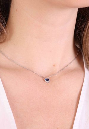 Zilveren ketting met een hartvormige blauwe edelsteen hanger, omringd door kleine heldere accenten. Gladde textuur, verfijnd ontwerp.