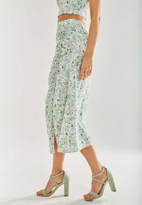 Floral maxi skirt in light green with pink accents, featuring a side slit and gathered design. Paired with mint green heeled sandals.