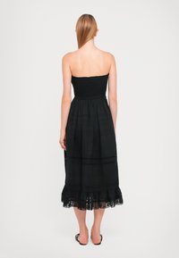 Vestido preto sem alças com corpete franzido, saia fluida até ao joelho e rendas na bainha. Tecido suave e leve.