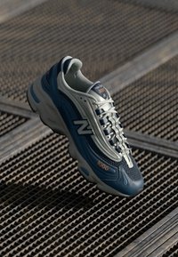 Blue and gray athletic shoe with mesh and synthetic materials, featuring a textured sole, embroidered branding, and a streamlined design.