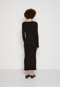 Robe longue noire en maille côtelée avec une silhouette ajustée, manches longues et un ourlet contrastant de couleur claire. Design simple, sans motifs.