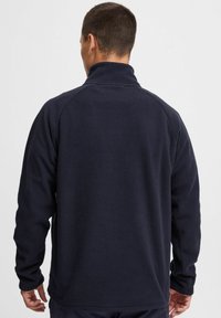 Sudadera de forro polar azul marino con un cuello alto y mangas raglán. Material texturizado y suave. Diseño simple, sin logotipos ni acentos visibles.
