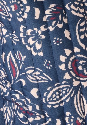 Tessuto trapuntato con sfondo blu scuro e motivi floreali in bianco e cremisi. La texture è liscia con cuciture visibili.