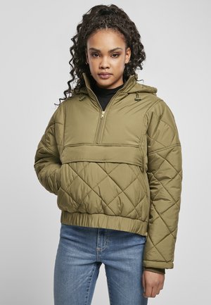Olivenfarget quiltet pullover-jakke med halv glidelås, snorhette, elastiske mansjetter og en frontlomme i kenguru-stil. Stilt med blå jeans.
