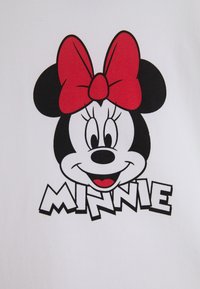 Tela blanca con un gráfico de un ratón de dibujo animado con orejas negras grandes, un moño rojo y el texto "MINNIE" en letras negras en negrita debajo.