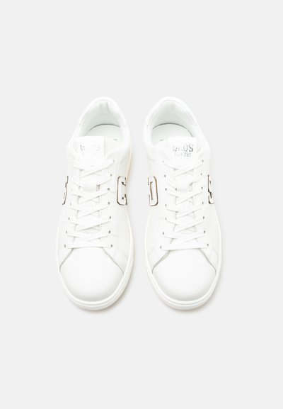 Paire de baskets basses blanches avec lacets et logos métalliques en forme de "G" sur les côtés, vues de dessus sur un fond blanc uni.
