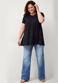 Schwarzes Baumwoll-T-Shirt mit ausgestelltem Saum, kombiniert mit hellblauen Schlagjeans. Das Outfit hat eine lockere Passform und kurze Ärmel.