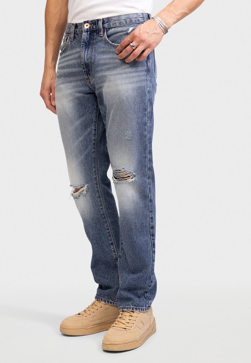 Lysblå slidte jeans med falmede områder og revne detaljer, parret med beige sneakers. Denim materiale, lige pasform.