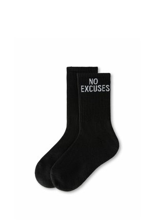 Paire de chaussettes noires côtelées avec la phrase "NO EXCUSES" en texte blanc près du haut du bord sur fond blanc.