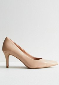 Zapato de tacón alto de charol nude con punta afilada y talón stiletto delgado, que presenta una textura suave y brillante.