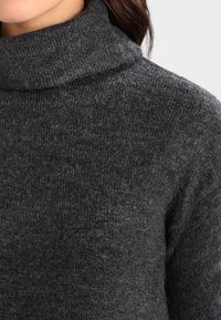 Pull à col roulé gris foncé en tissu tricoté texturé, doté d'un col ample et d'une apparence douce et chaude.