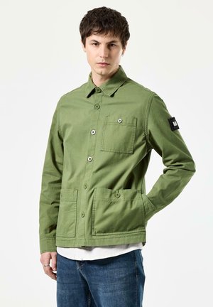 Green work jacket made of cotton, featuring a button-up front, two large front pockets, and a black patch on the left sleeve.