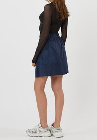 Jupe bleu marine avec taille élastique, fabriquée dans un tissu doux, longueur genoux, associée à un haut noir à manches longues et des baskets grises.