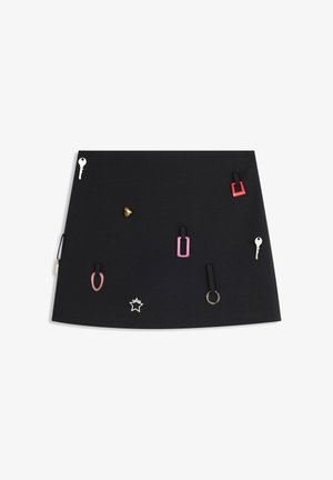 Schwarzer A-Linien-Rock mit befestigten dekorativen Metallanhängern in Form von Schlüssel, Stern, Kegel und Ring in Silber, Gold, Rot und Rosa.