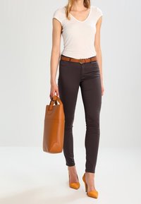 Brązowe obcisłe dżinsy, biała dopasowana koszulka, pomarańczowy pasek, dopasowana pomarańczowa torba na ramię i żółte szpilki. Gładkie faktury i czyste linie.