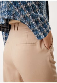 Beiga byxor med bakfickor, kombinerade med en strukturerad topp i blått och gräddvitt vävt tyg. Outfitten är åtsittande och visar upp rena linjer.