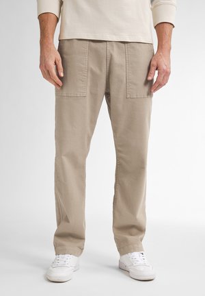 Pantalones de algodón beige con dos bolsillos frontales, diseño recto y un corte relajado, combinados con zapatillas blancas.