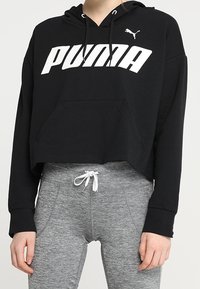 Felpa corta nera con logo bianco "PUMA", cappuccio regolabile con cordino e tasca frontale, abbinata a leggings sportivi grigi.