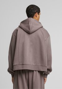 Felpa oversize marrone in materiale morbido, con una grande cappuccio, cuciture delle spalle cadenti e polsini a costine, caratterizzata da una vestibilità morbida.