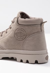 Bota de senderismo beige con parte superior de cuero texturizado, puntera redondeada, talón reforzado y suela de goma con un patrón de banda de rodadura distintivo.