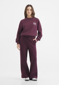 Bordeaux trui en wijde broek set, gemaakt van zachte stof. De trui heeft een ronde halslijn en een logo detail aan de voorkant. De broek heeft een elastische taille.