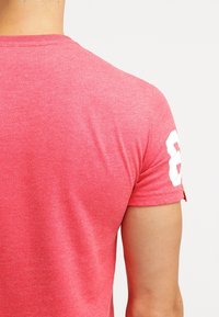 Maglietta aderente a maniche corte in tessuto rosso brillante. Presenta il numero 8 bianco sulla manica sinistra, una trama liscia e un design con collo rotondo.