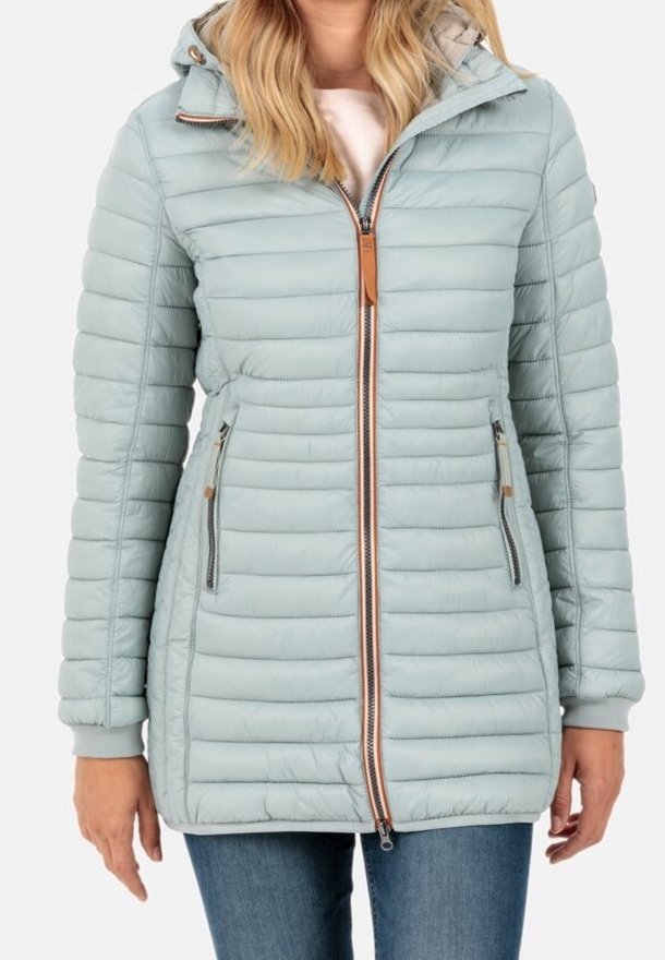 Mujer vistiendo una chaqueta acolchada con capucha de color azul claro, con cremallera frontal y bolsillos laterales con cremallera, combinada con jeans azules.