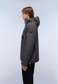 Grijze hoodie gemaakt van glad, waterafstotend materiaal, voorzien van een patch op de linkerarm en verstelbare trekkoorden. Zijaanzicht.