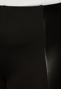 Black pants featuring a combination of matte fabric and shiny leather-like side panels, with a smooth texture and tailored fit.