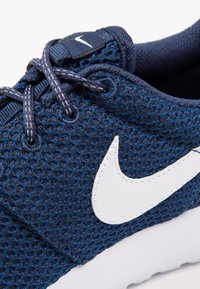 Laivaston verkkomallinen urheilusandaali valkoisella Nike-logolla, tekstuuripinta, tasaiset nauhat ja pehmustettu nilkkaosa. Valkoinen pohja, jossa on kevyt kaarevuus varpaissa.