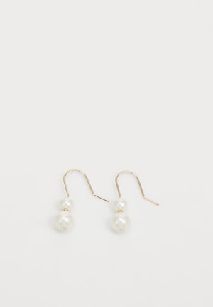Boucles d'oreilles à crochet doré avec deux perles blanches empilées sur chacune, la perle plus petite au-dessus de la plus grande, sur un fond blanc uni.
