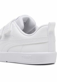 Chaussure de sport blanche avec tige en cuir synthétique, col rembourré et sangle Velcro. Présente des accents texturés et un logo sur le côté et le talon.