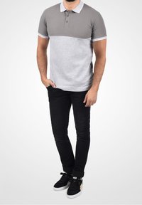 Polo gris et gris clair avec col, deux boutons et manches courtes ; associé à un jean noir et des baskets noires avec des accents dorés.