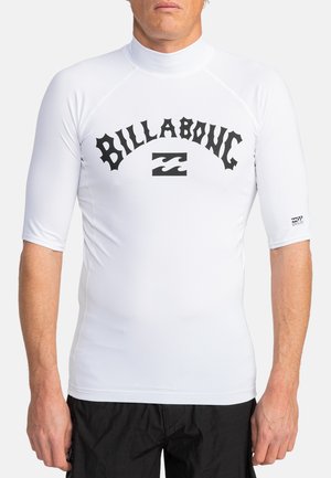Hvid langærmet rash guard lavet af strækbart materiale, der har et fremtrædende sort "BILLABONG" logo og bølgediagram på forsiden.