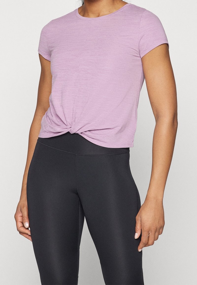 Lyserød kortærmet t-shirt med knot-design fortil, kombineret med højtaljede sorte leggings lavet af glat, strækbart stof.