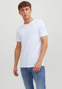 T-shirt en coton blanc avec un col rond, des manches courtes et une coupe décontractée. Associé à un jean en denim bleu clair. Design simple, sans motifs.
