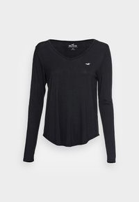 Černé tričko s dlouhým rukávem a výstřihem do V, vyrobené z měkkého materiálu, s jemným malým logem na levé části hrudi a zaobleným lemem.