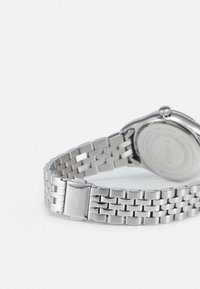 Montre-bracelet en métal argenté avec un bracelet tissé. Le dos présente des détails gravés et un boîtier rond. Le fermoir est marqué du nom de la marque, "Timex."