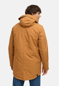 Brūna, polsterēta parka jaka ar kapuci, ar taisnu piegriezumu, sānu kabatām un smalku teksturētu audumu. Jaka līdz viduklim ar aizmugurēju venti.