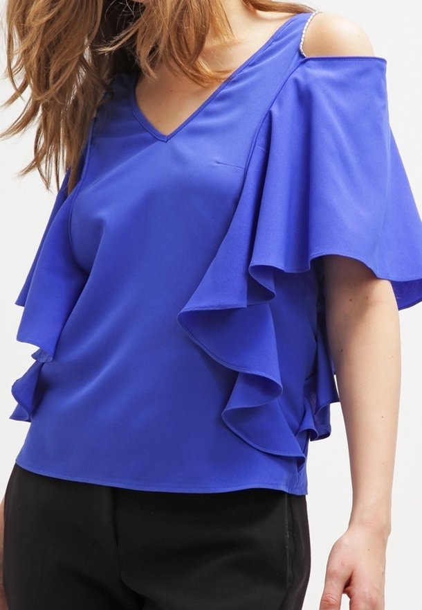 Blå blus med V-ringning, volangärmar och kall axel-design. Slät tyg med flytande fall; har en subtil lyster.