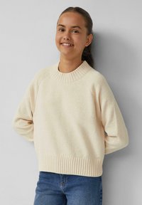 Lichtbeige trui met een geribbelde halslijn en zoom. Heeft een gestructureerde breipatroon en een relaxte pasvorm. Gecombineerd met blauwe jeans.