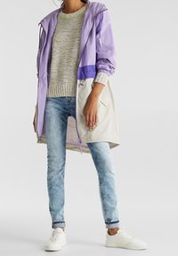 Lättviktig, lila och beige huva-jacka över en flerfärgad stickad tröja, sammansatt med ljusblå denim och vita sneakers.