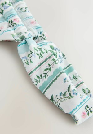 Čelenka s kvetinovým vzorom, ktorá kombinuje modré, ružové a zelené kvety na bielom pozadí, s horizontálnymi pruhmi a vlnitými okrajmi.