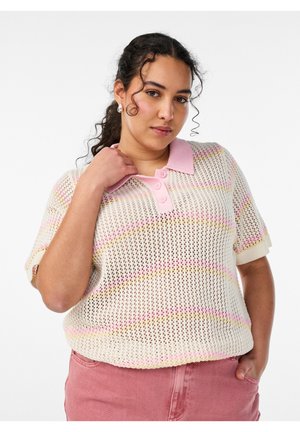 Žena s kučeravými vlasmi oblečená v krémovom krátkym rukávom polosviatku s ružovými pruhmi, ružovým golierom a ružovými nohavicami, stojaca s jednou rukou v vrecku.