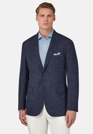 Marineblauer Leinenmix-Blazer mit strukturierter Oberfläche, mit Revers und zwei Fronttaschen. Kombiniert mit einem hellblauen Poloshirt und weißen Hosen.