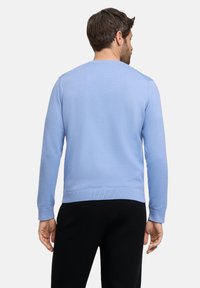 Maglione a maglia blu chiaro con collo a giro, polsini e orlo a coste, texture liscia e dettagli minimali, abbinato a pantaloni neri.