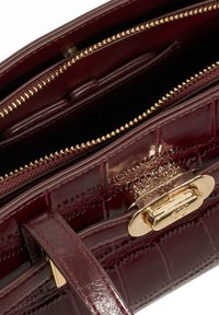 Burgundy faux-crocodile leather handbag with gold-tone hardware and zippers. Features multiple compartments for organization.